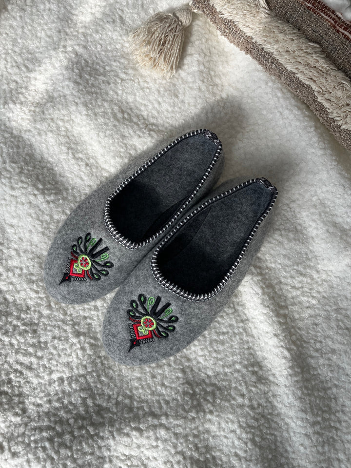 Pair of gray slippers with floral embroidery on a textured surface