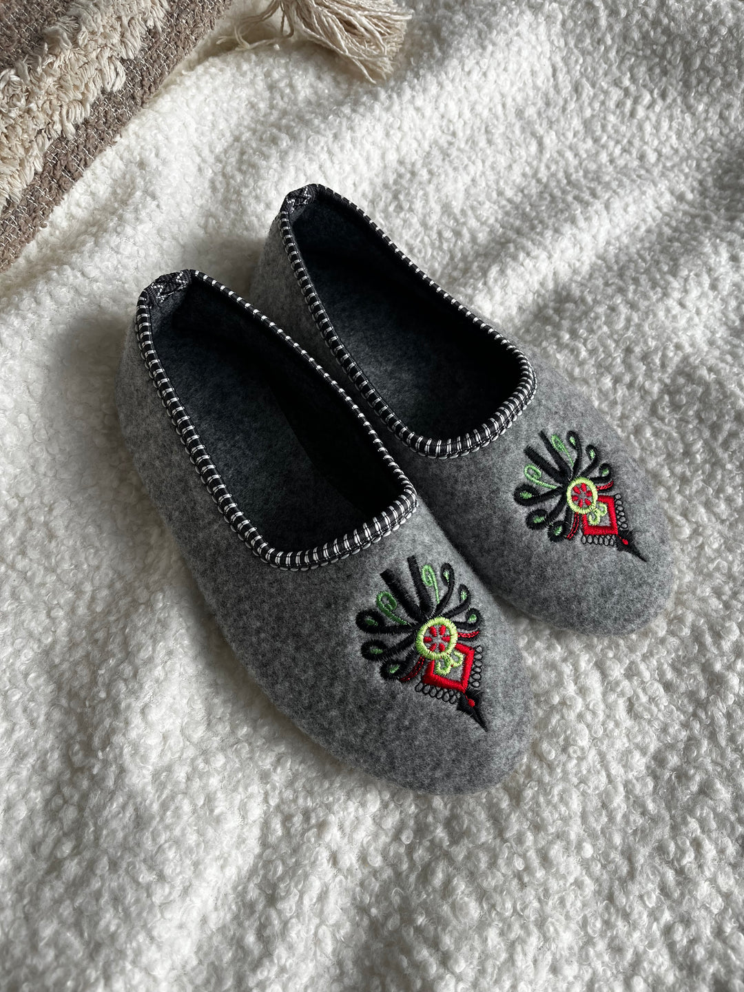 Pair of gray slippers with decorative patterns on a white blanket