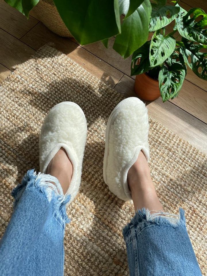 Person wearing white slippers on a wooden floor with a plant in the background