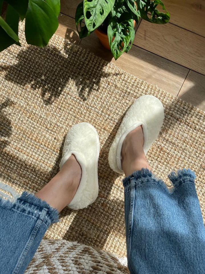 White slippers worn on a woven mat with a plant in the background