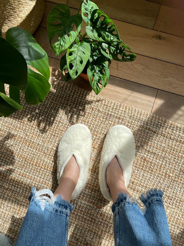 White slippers on a woven mat with plants in the background