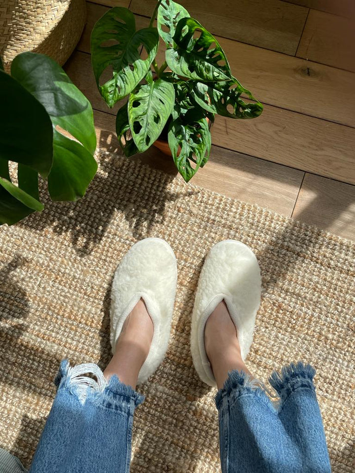 White slippers on a woven mat with plants in the background