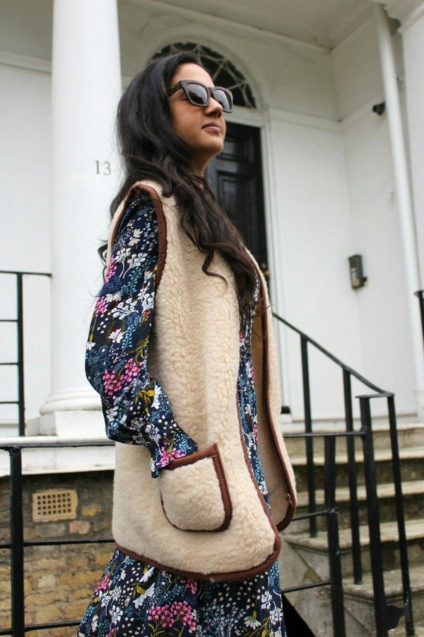 Woman wearing a floral top and beige vest outdoors.