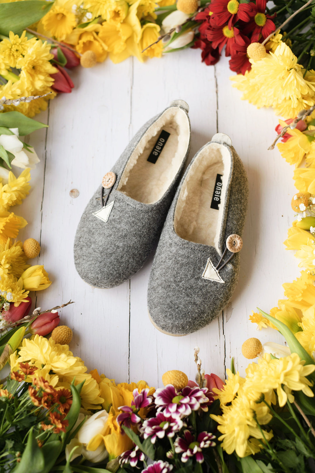 Gray slippers on a white wooden surface surrounded by yellow flowers.